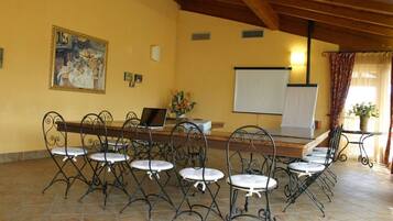 A dining area with a long table and six chairs, a whiteboard, and a painting on the wall.