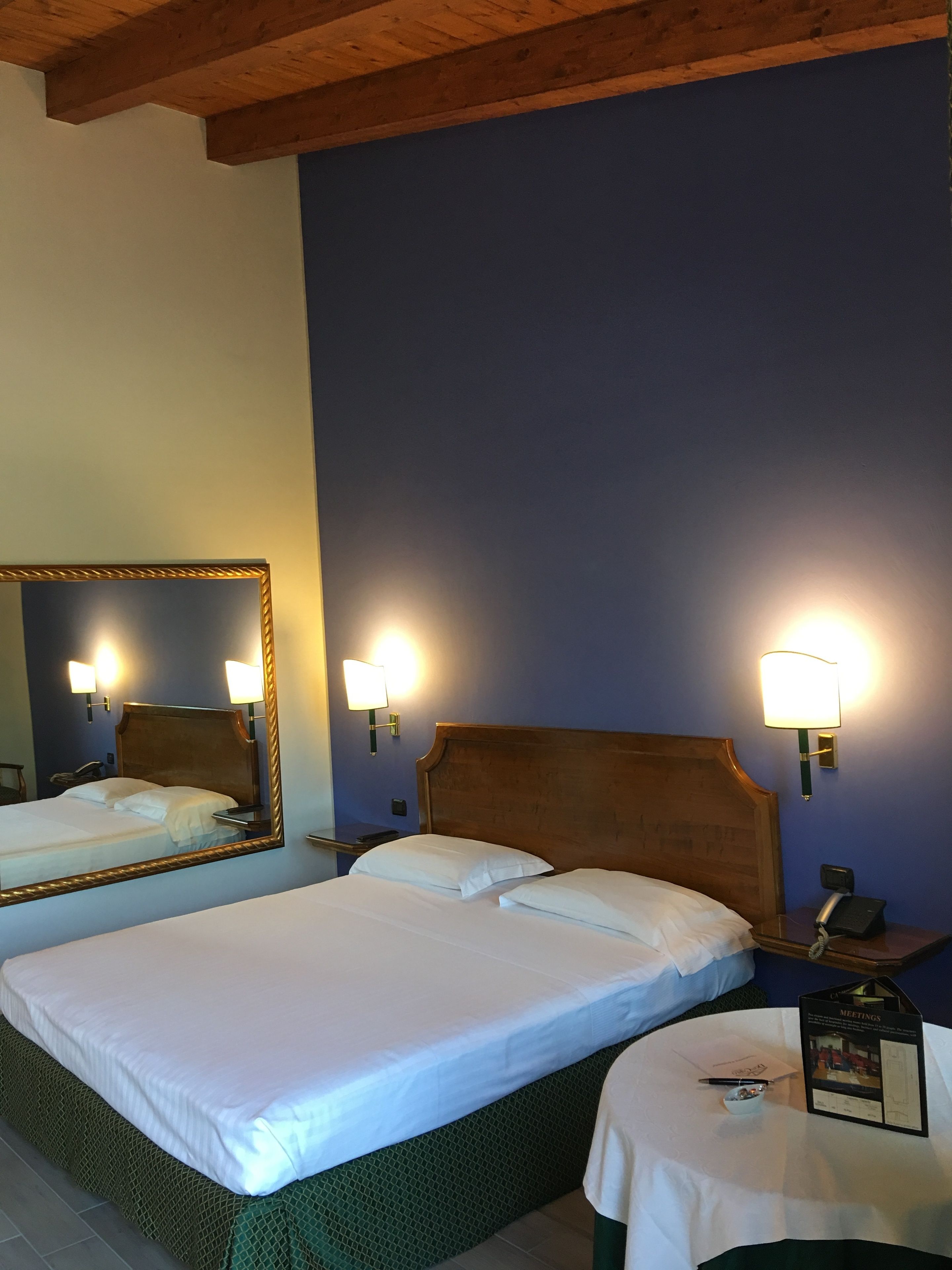 A hotel room with two beds, a large mirror, bedside lamps, a telephone, a small table with a menu, and a framed picture on the wall.