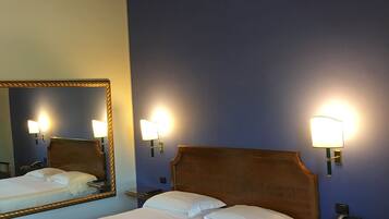 A hotel room with two beds, a large mirror, bedside lamps, a telephone, a small table with a menu, and a framed picture on the wall.