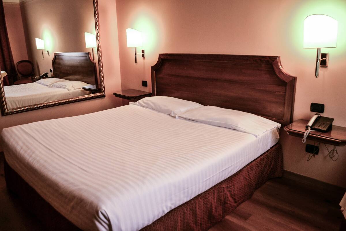 A hotel room with a large bed, a bedside table with a lamp, a mirror, and a phone on the nightstand.
