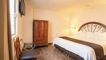 Quarto com guarda-roupa de madeira, cama com roupa de cama branca e escura, uma cadeira e um abajur na parede.