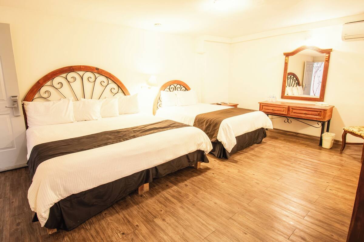 Habitación de hotel con dos camas, suelo de madera, cómoda y espejo.