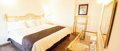 A hotel room with a bed, bedside table, and a mirror.