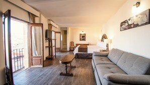 Quarto de hotel com piso de madeira, um sofá, uma cama, uma escrivaninha e uma cadeira.