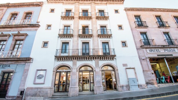 Fachada de hotel com entrada central, varandas e um letreiro com a inscrição 'Hotel Posada'.