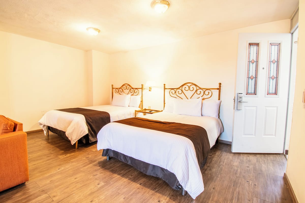 Habitación de hotel con dos camas, piso de madera, una puerta blanca con vidrieras y una pequeña mesa entre las camas.