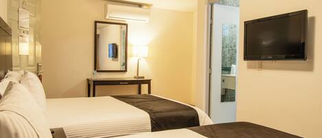A hotel room with two beds, a desk, a mirror, a TV, and a door leading to a balcony.