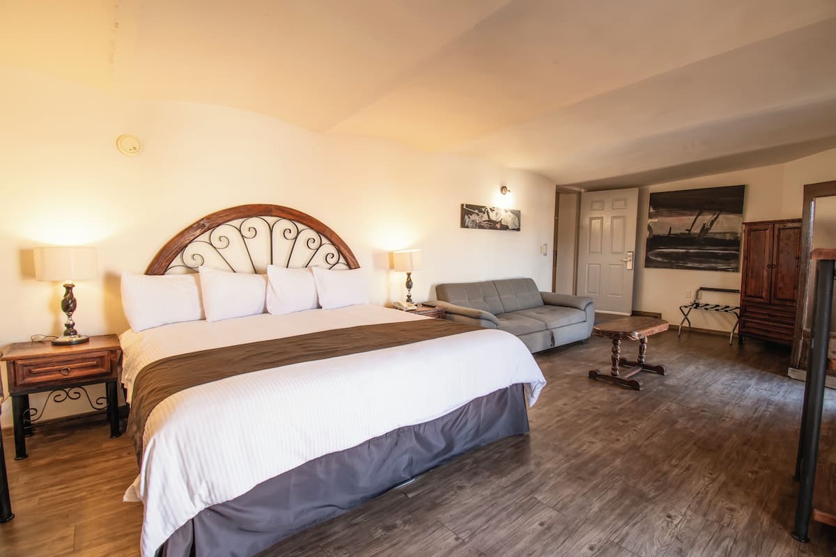Un dormitorio con una cama grande, un sofá gris, una mesita y un armario de madera.