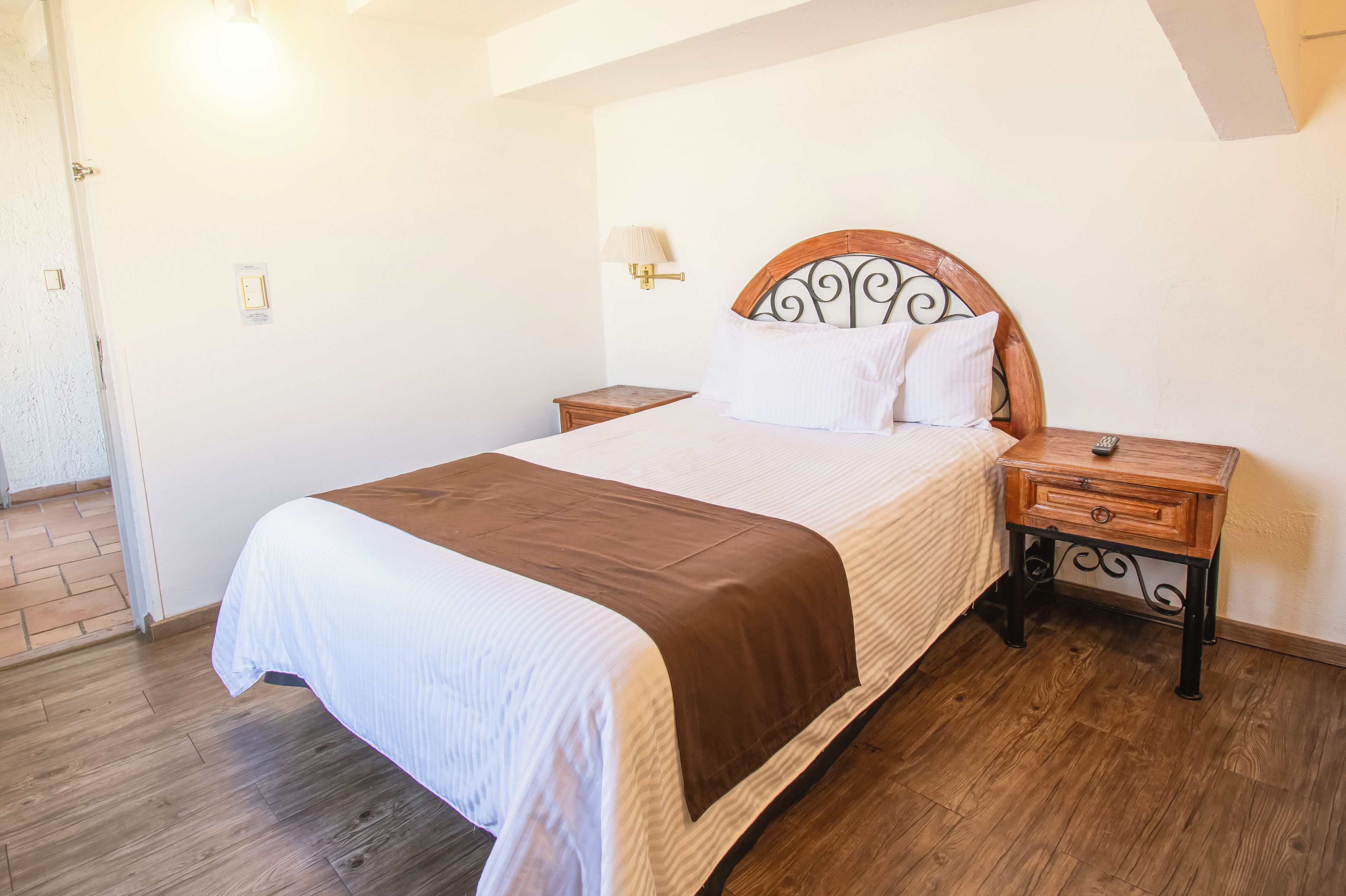 A neatly made bed with a wooden headboard, a bedside table with a lamp, and a wooden floor.