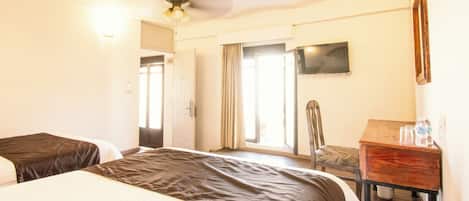 Habitación de hotel con dos camas, ventilador de techo, televisión y un escritorio de madera con una silla.