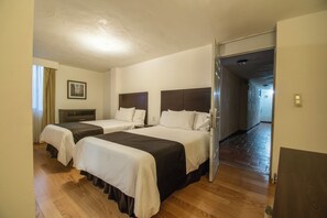 Habitación de hotel con dos camas, piso de madera y un pasillo que conduce a otra habitación.