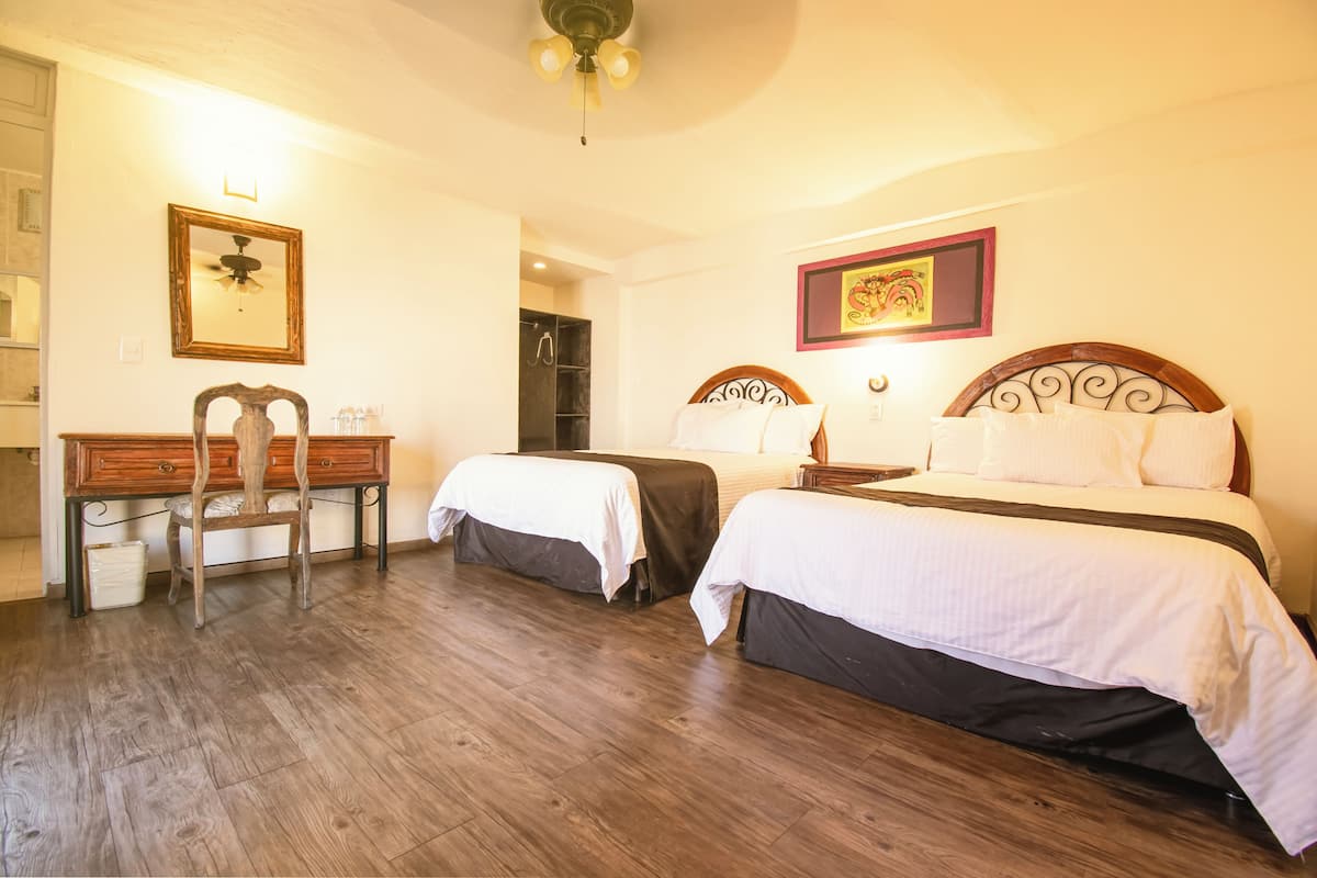 Habitación de hotel con dos camas, un escritorio, una silla, ventilador de techo y zona de ducha.