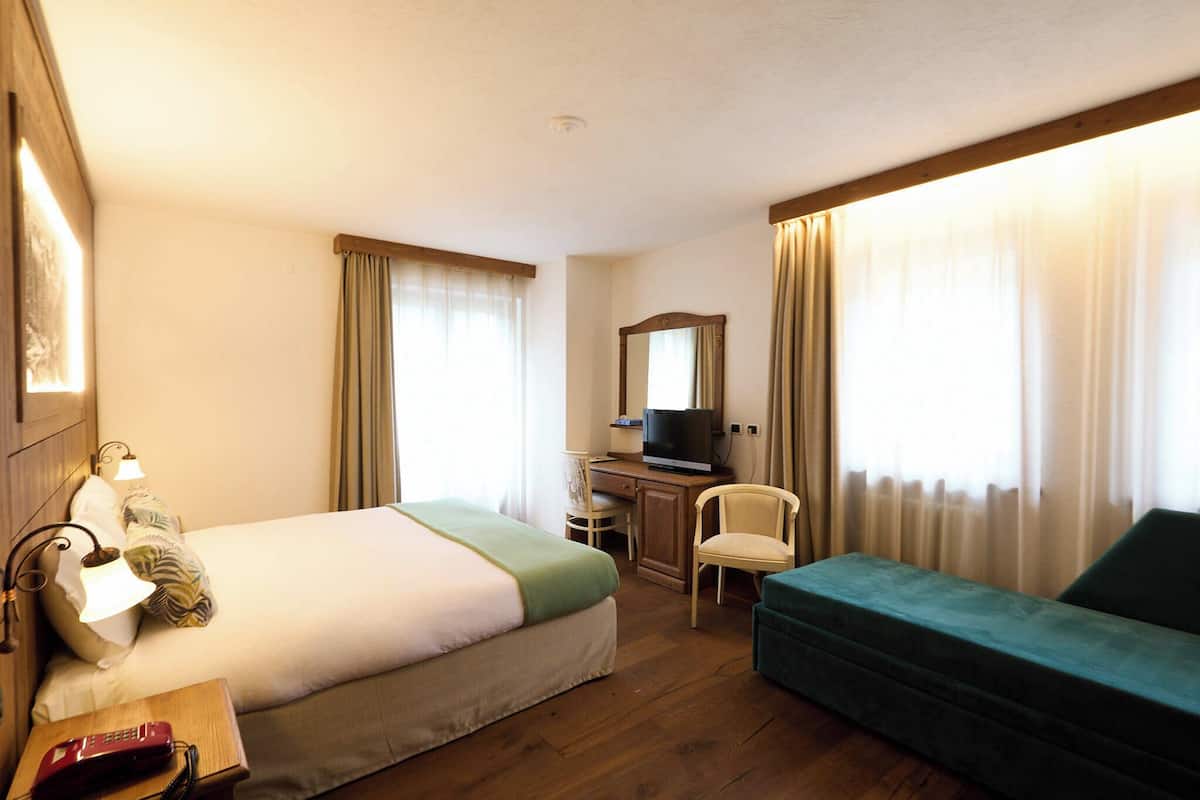 A hotel room with a bed, a desk with a television, a chair, and a sofa.