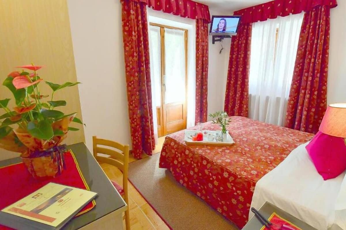 A hotel room with a bed, a desk with a lamp, a television, and a window with curtains.