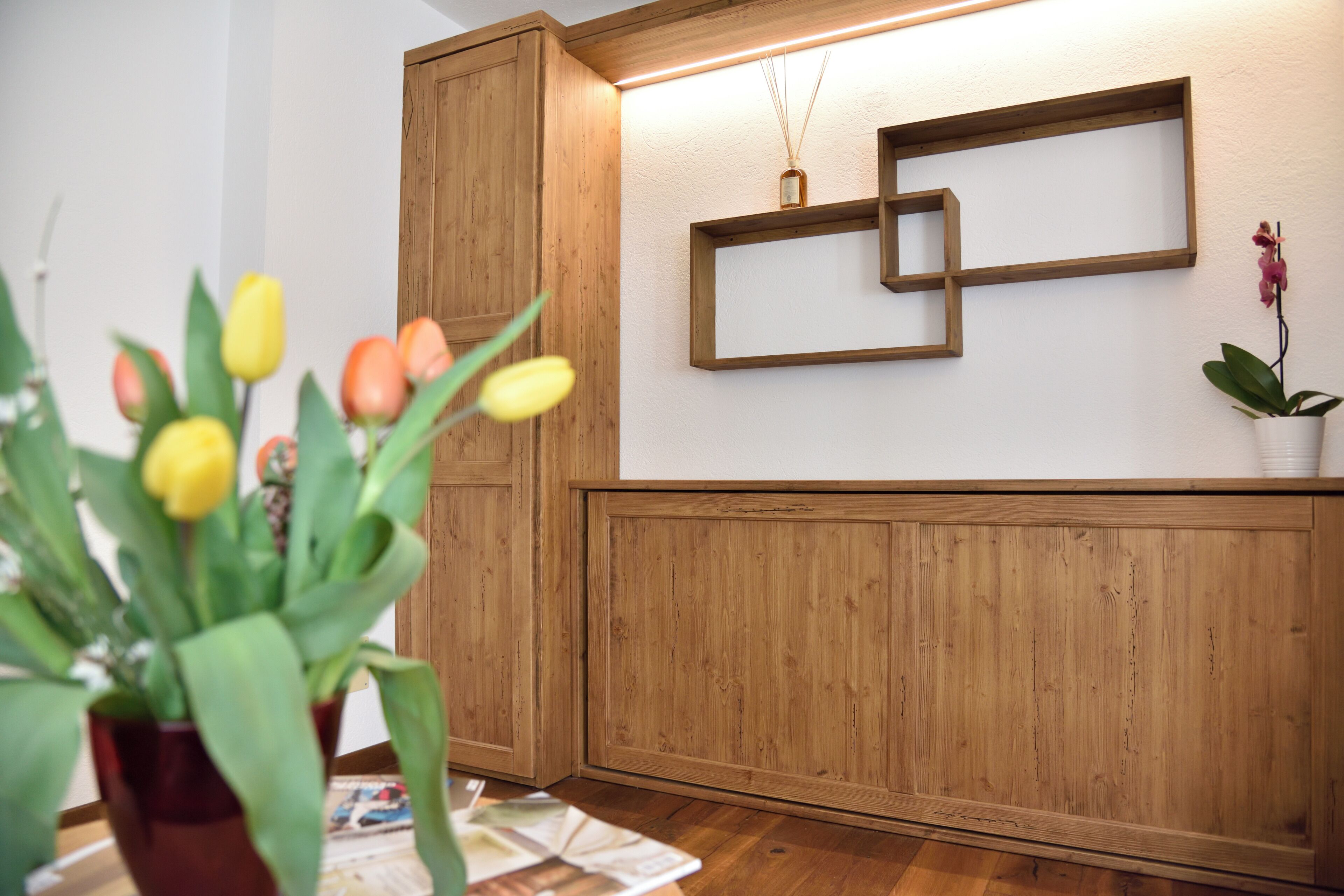 A wooden panel wall with a shelf, a potted plant, and a vase with a reed diffuser.