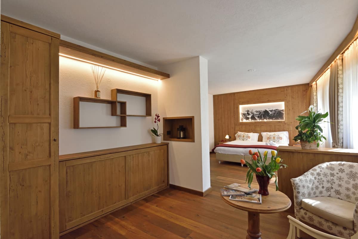 A room with wooden paneling, a bed with white bedding, a window with curtains, and a potted plant on a table.