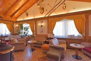 A cozy room with wooden ceilings, plush seating, a fireplace, and hunting trophies. - Hotel Beau Sejour (Etroubles)