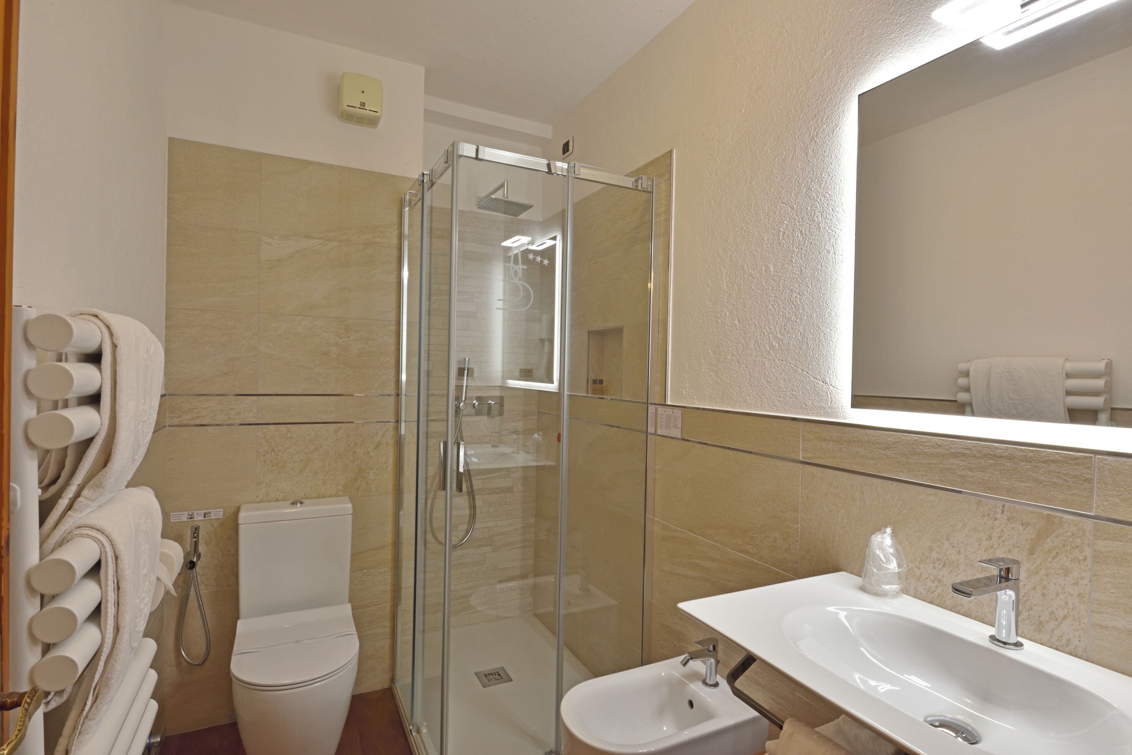 A bathroom with a glass-enclosed shower, a toilet, a bidet, and a sink with a mirror above it.