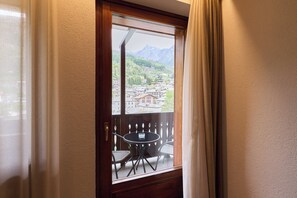 Una stanza con un balcone, un tavolo con sedie e vista su una città e montagne.