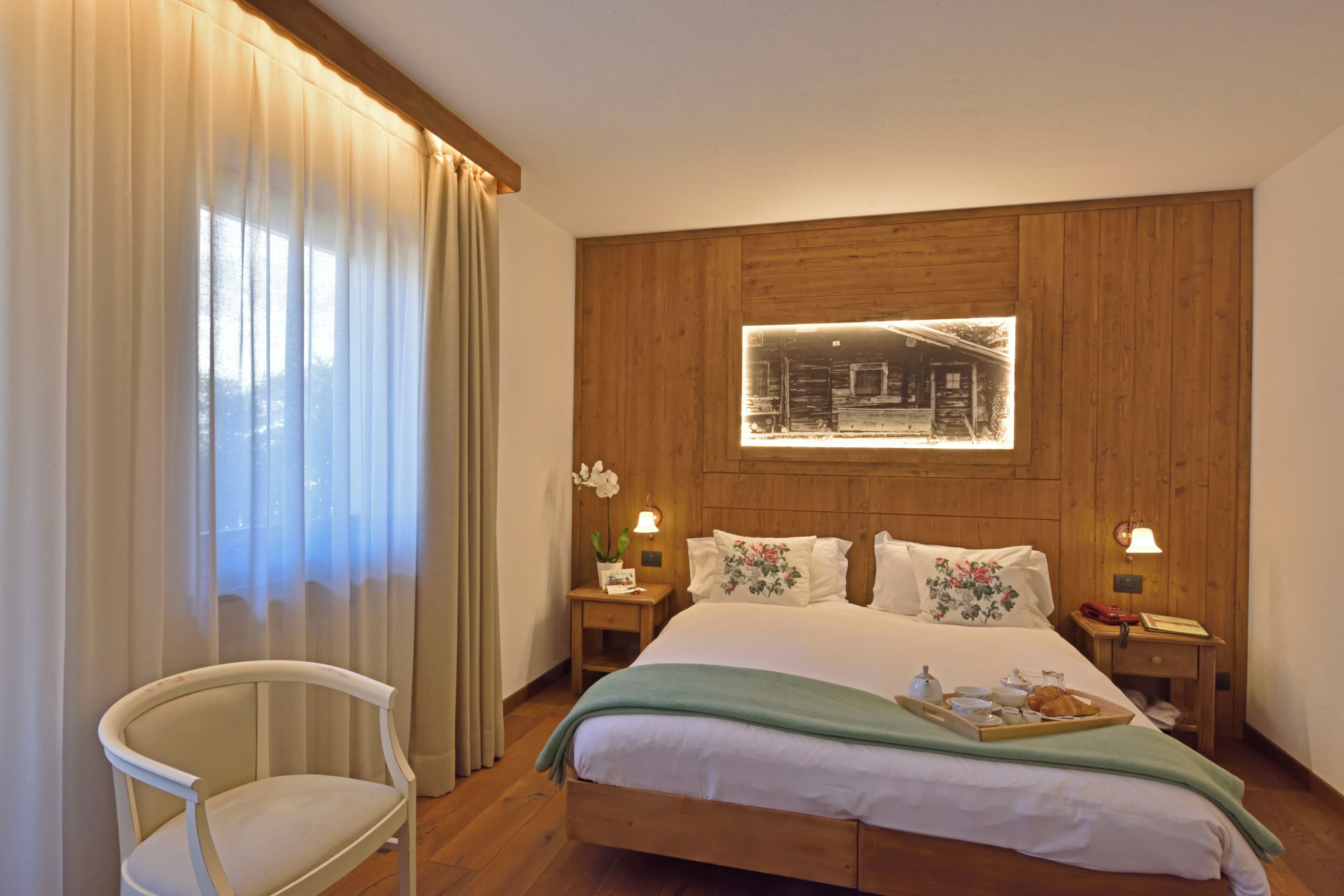 Ein Hotelzimmer mit einem hölzernen Kopfteil, einem Bett mit floralen Kissen, einem Nachttisch mit Lampe und einem Sessel.