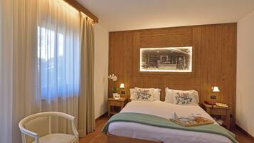 Ein Hotelzimmer mit einem hölzernen Kopfteil, einem Bett mit floralen Kissen, einem Nachttisch mit Lampe und einem Sessel.