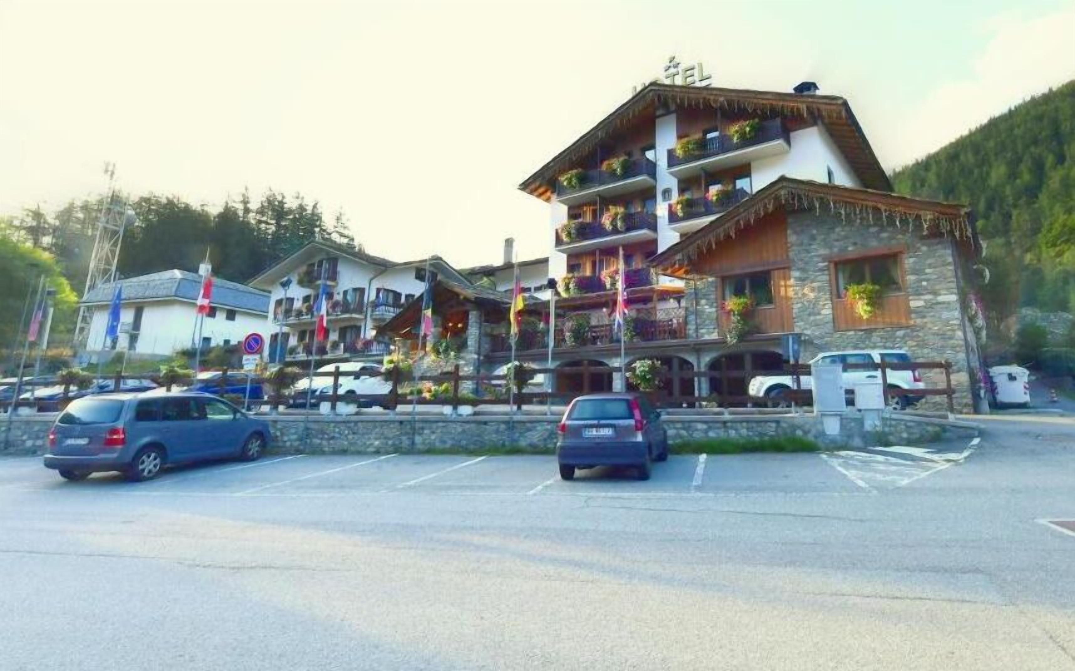 A multi-story hotel with balconies, a stone facade, and a parking lot with cars.