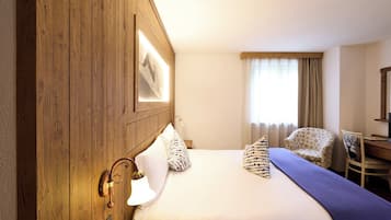 Une chambre d’hôtel avec une tête de lit en bois, un lit avec une literie blanche, une chaise, un bureau et une fenêtre avec des rideaux.