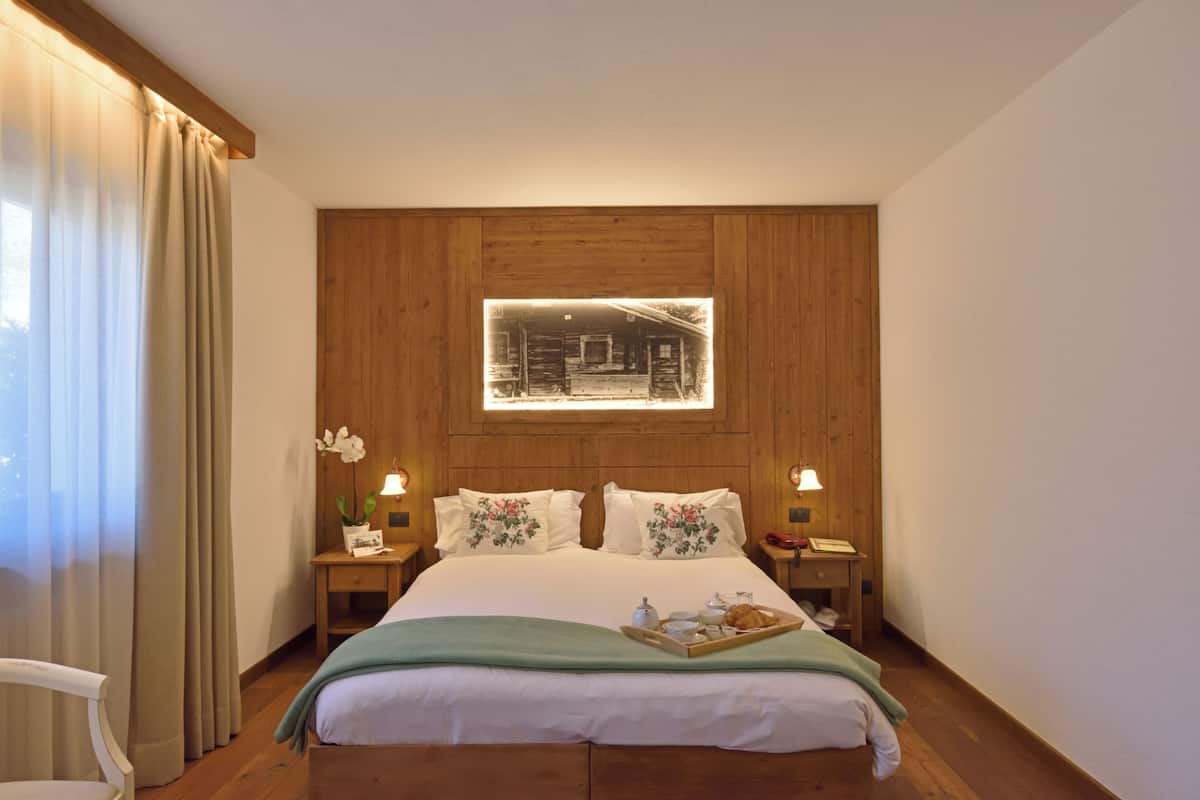 A neatly arranged bedroom with a wooden headboard, a bedside table with a lamp, and a window with curtains.