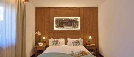 A neatly arranged bedroom with a wooden headboard, a bedside table with a lamp, and a window with curtains.