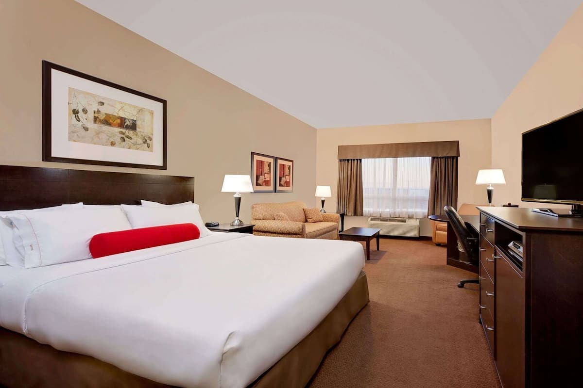 Habitación de hotel con una cama grande, un sofá, un escritorio, un televisor y una ventana con cortinas.
