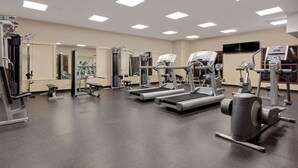 Un gimnasio con diversas máquinas de ejercicio, incluyendo cintas de correr y máquinas de pesas, y un espejo grande en la pared.