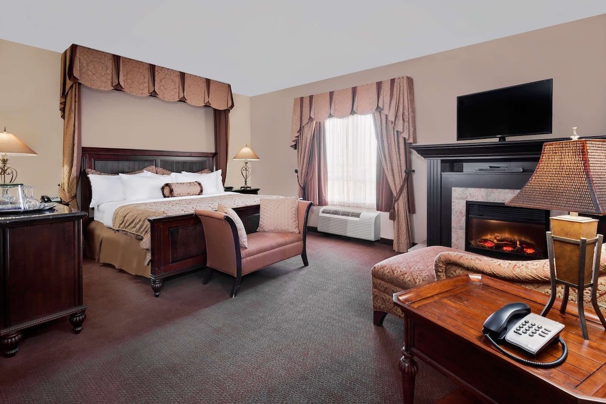 Habitación de hotel con una cama grande, un escritorio con teléfono, una chimenea y un televisor montado en la pared.