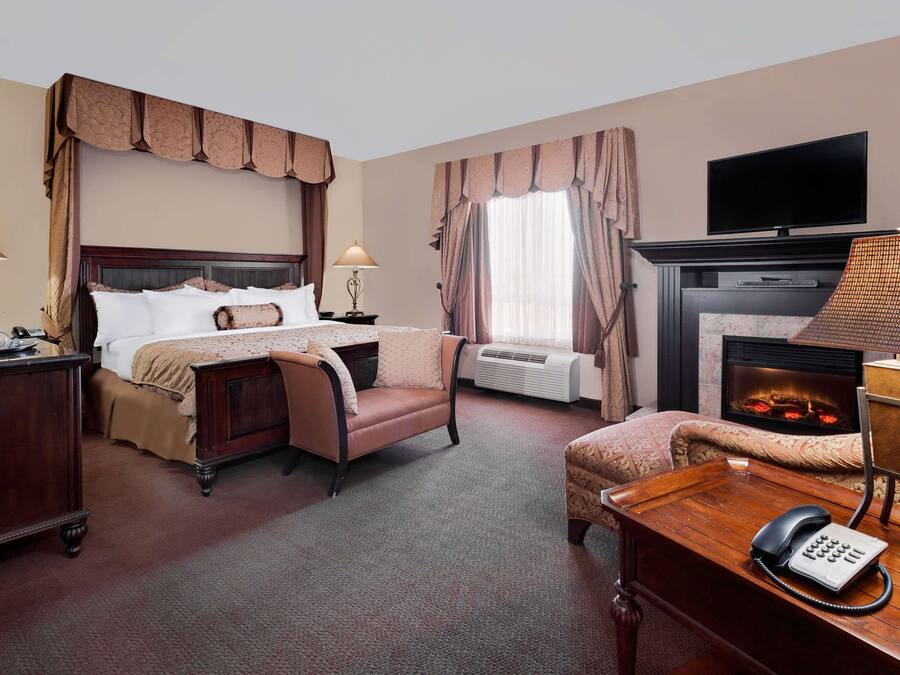 A hotel room with a large bed, a desk with a telephone, a fireplace, and a television mounted on the wall.