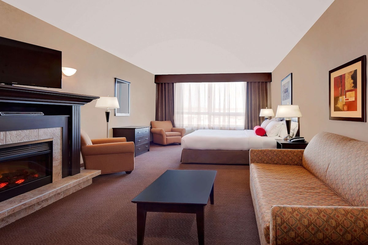 Una habitación de hotel con chimenea, una cama, un sofá, un escritorio y un televisor.