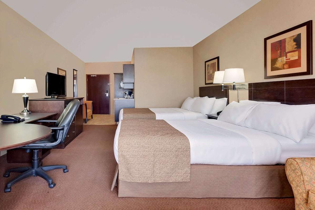 Habitación de hotel con escritorio, dos camas, televisor y kitchenette.
