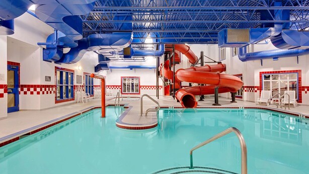 Una piscina interior con un tobogán de agua rojo y tuberías de techo azules.