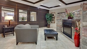 Una sala de estar moderna con sofá, reposapiés y chimenea. Hay espejos, una lámpara y una planta en maceta.