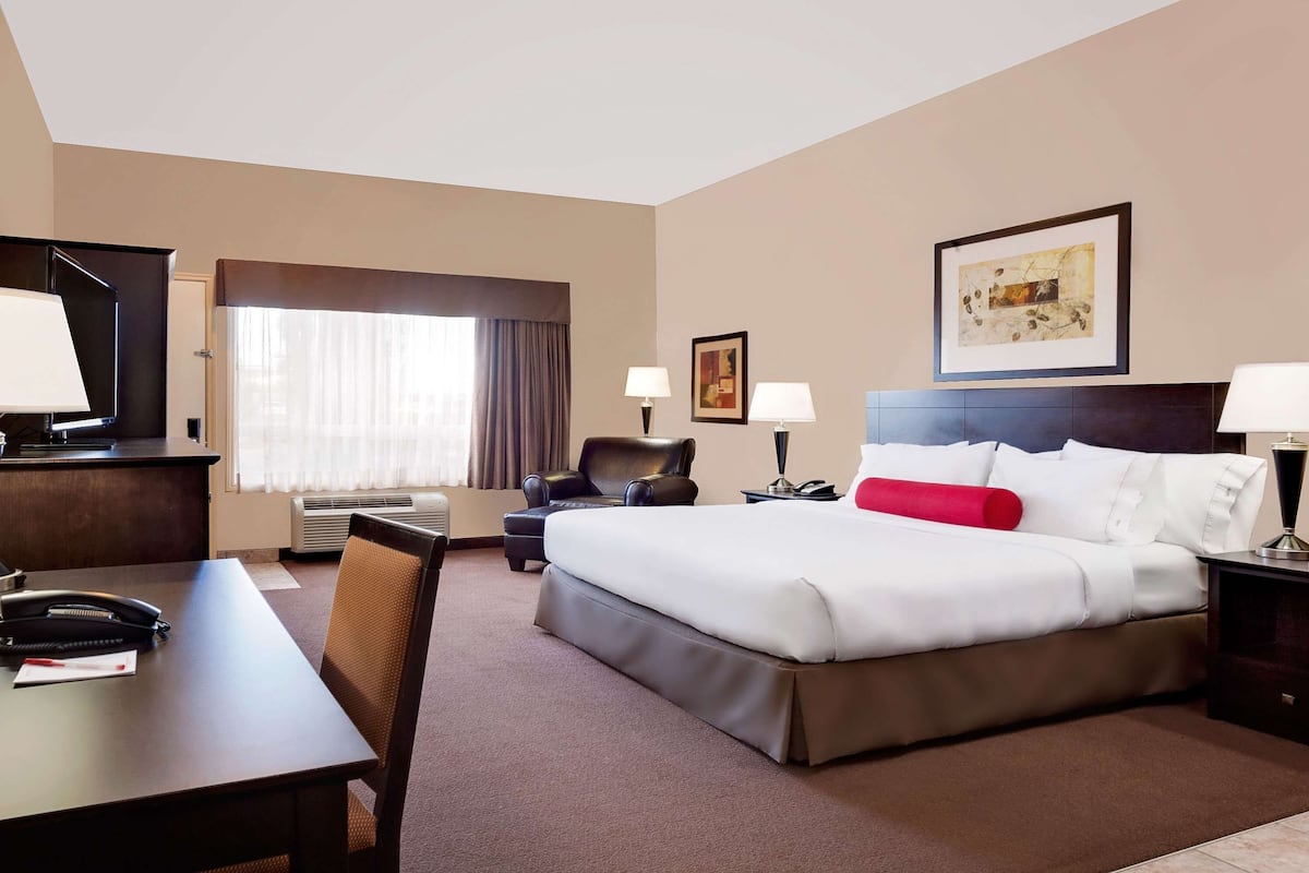 Una habitación de hotel con una cama, un escritorio, una silla, un televisor y un ventanal con cortinas.
