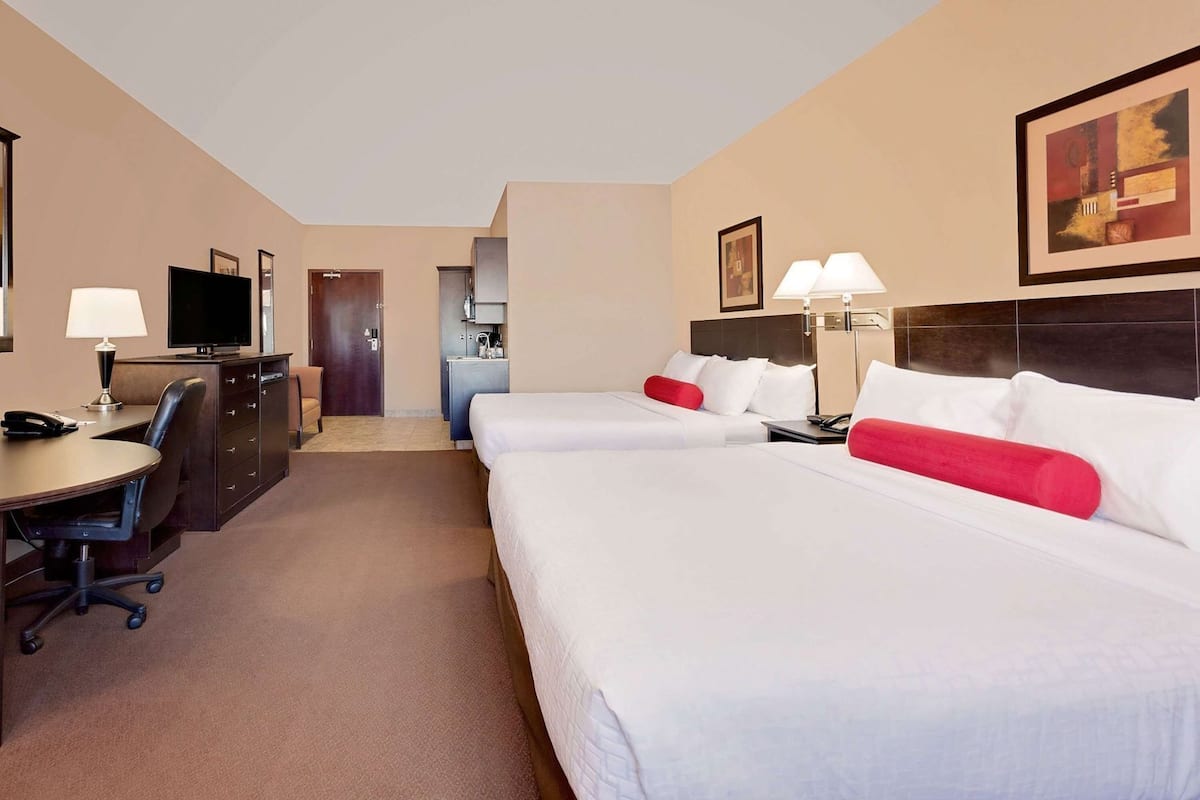 Habitación de hotel con dos camas, un escritorio, una silla, un televisor y una kitchenette pequeña.