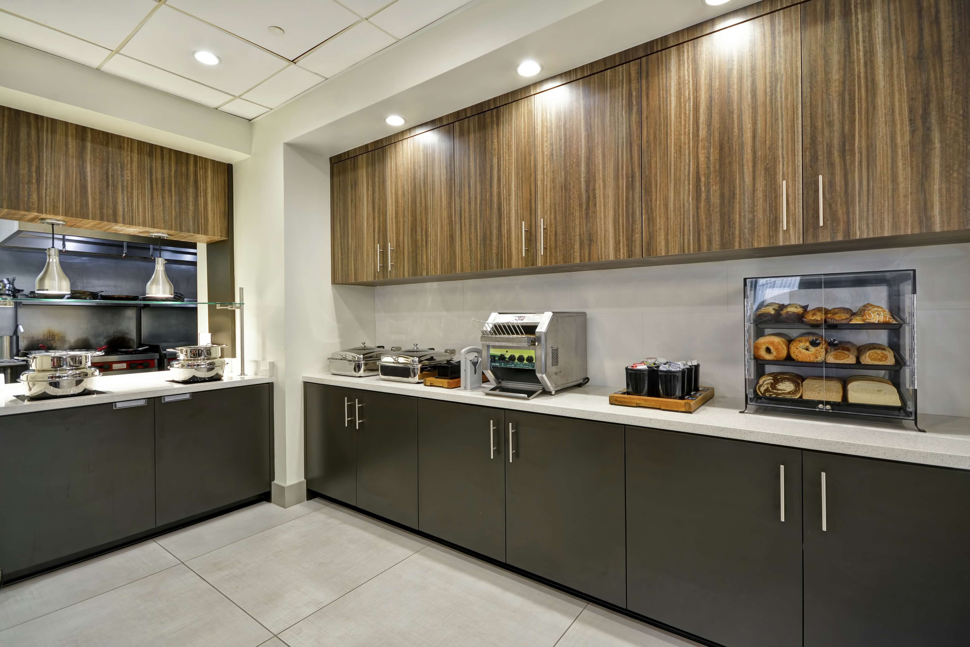 A modern kitchen with dark cabinets, a countertop with various appliances, and a display case with baked goods.