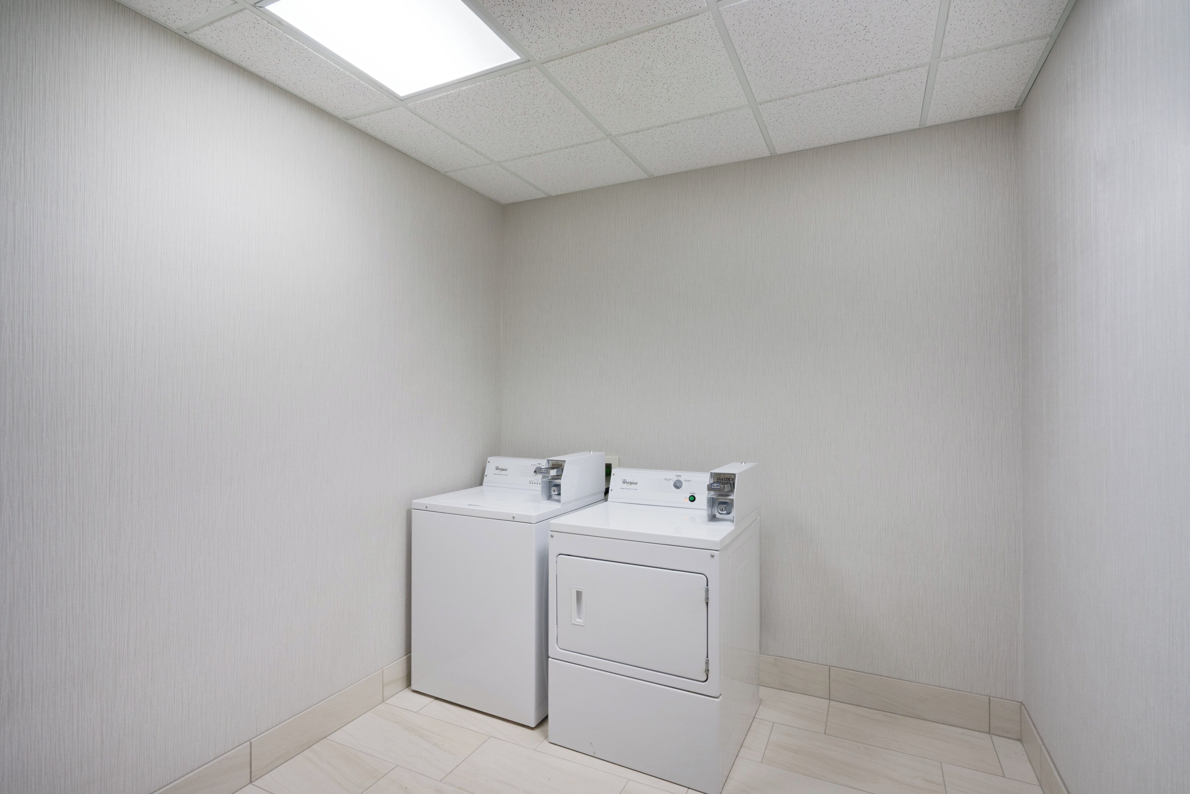 A laundry room with two stacked washers and dryers, a tiled floor, and a ceiling with a skylight.