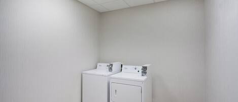 A laundry room with two stacked washers and dryers, a tiled floor, and a ceiling with a skylight.
