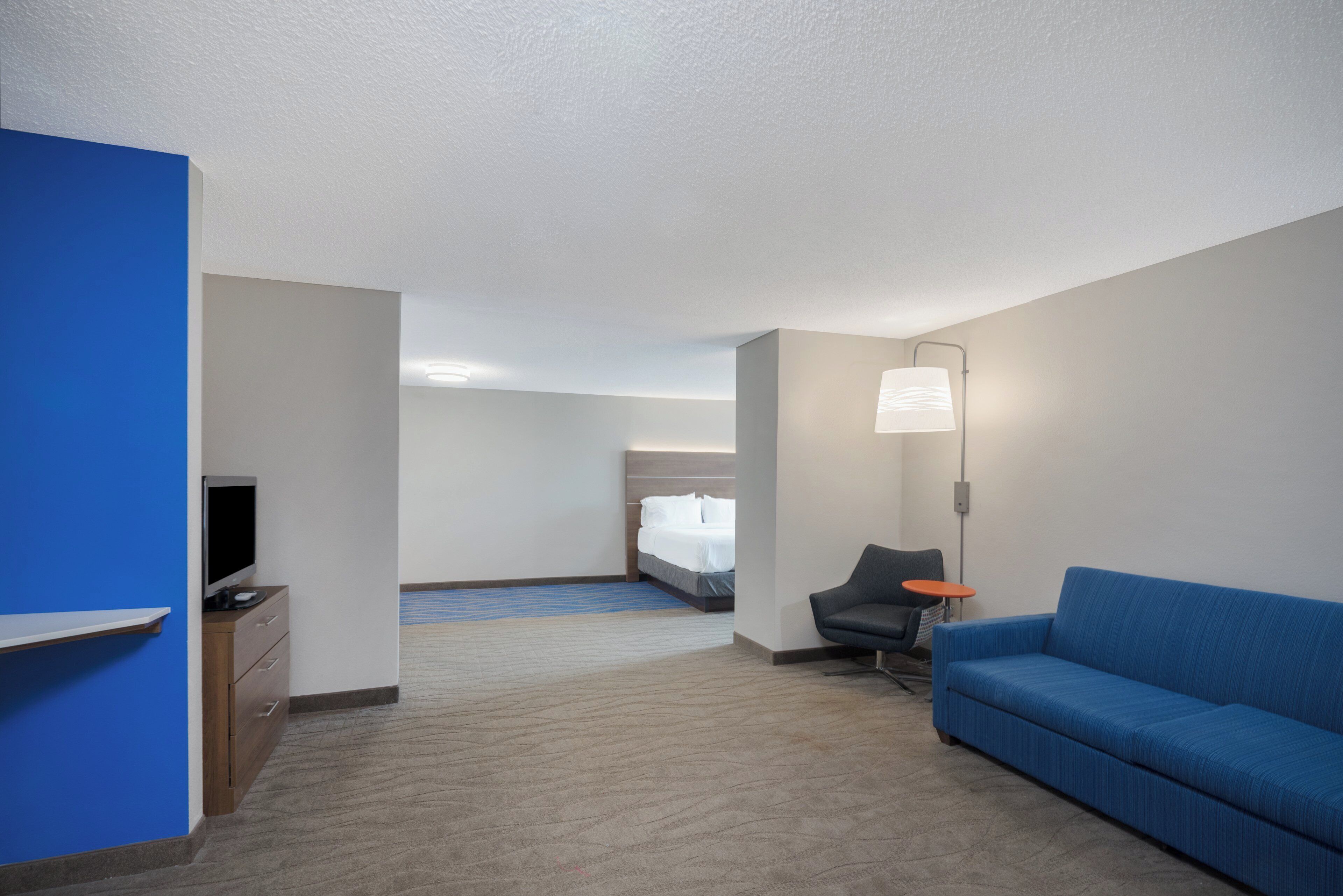 Ein Hotelzimmer mit einem blauen Sofa, einem Schreibtisch mit Fernseher, einem Bett und einem kleinen Tisch mit Lampe.