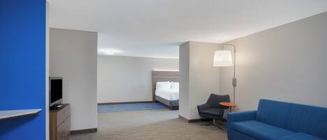 Ein Hotelzimmer mit einem blauen Sofa, einem Schreibtisch mit Fernseher, einem Bett und einem kleinen Tisch mit Lampe.