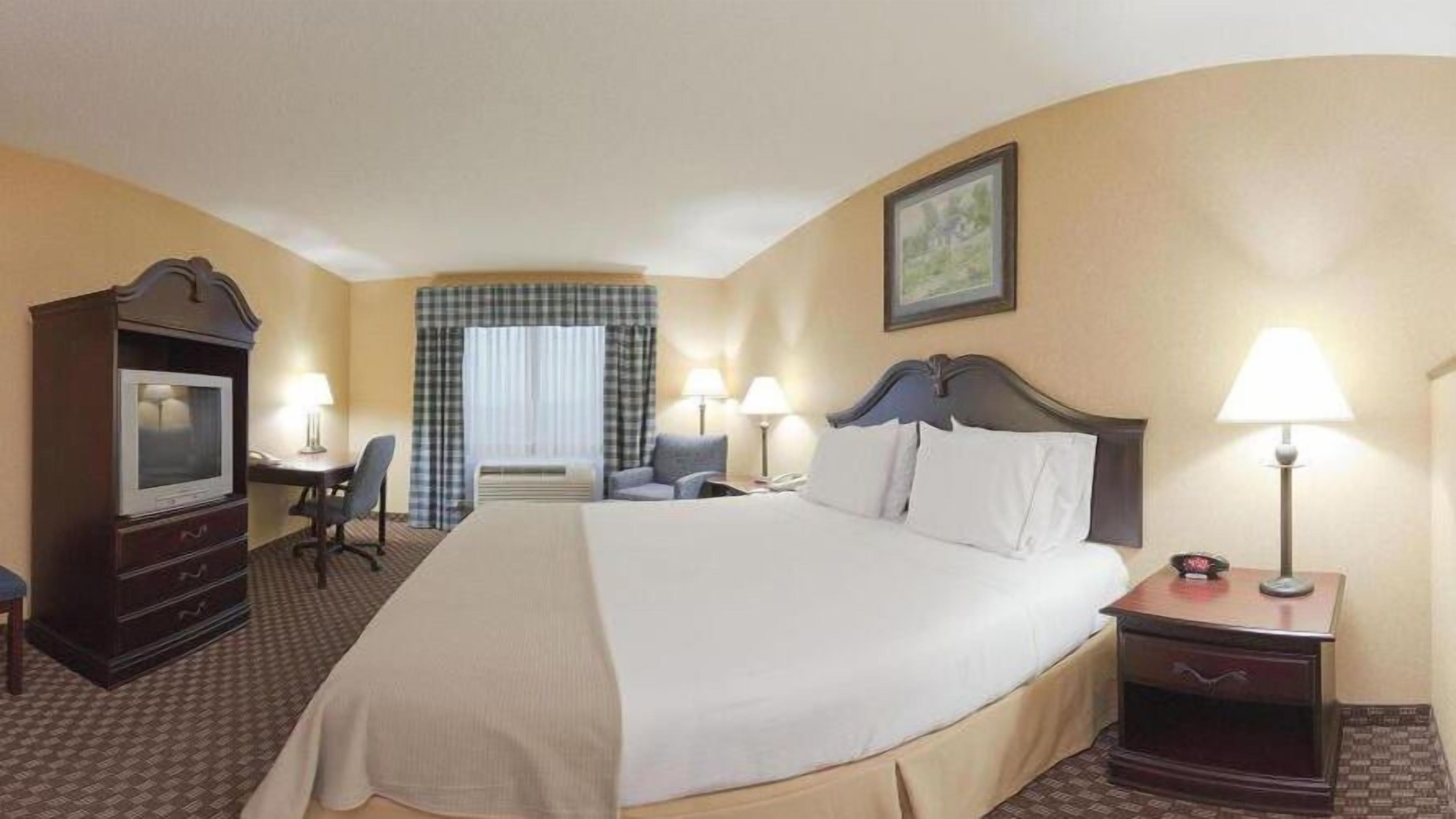 A hotel room with a large bed, a desk with a chair, a television, and a window with curtains.