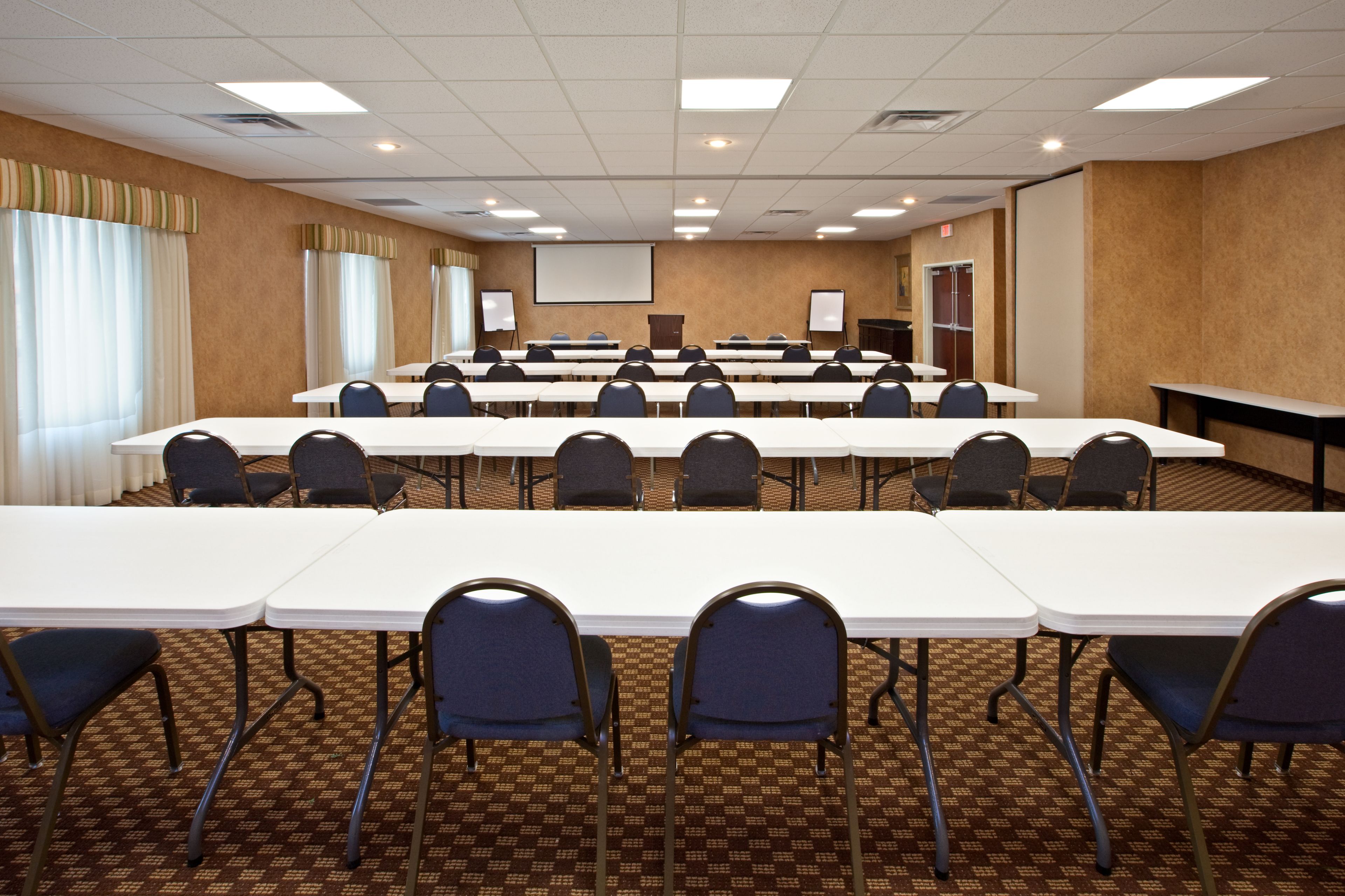 Une salle de conférence équipée de plusieurs tables et chaises, d’un écran de projection et d’un tableau de présentation.