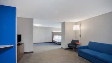 Una habitación de hotel con un sofá azul, un escritorio con televisor de pantalla plana, una cama y una mesita de noche.