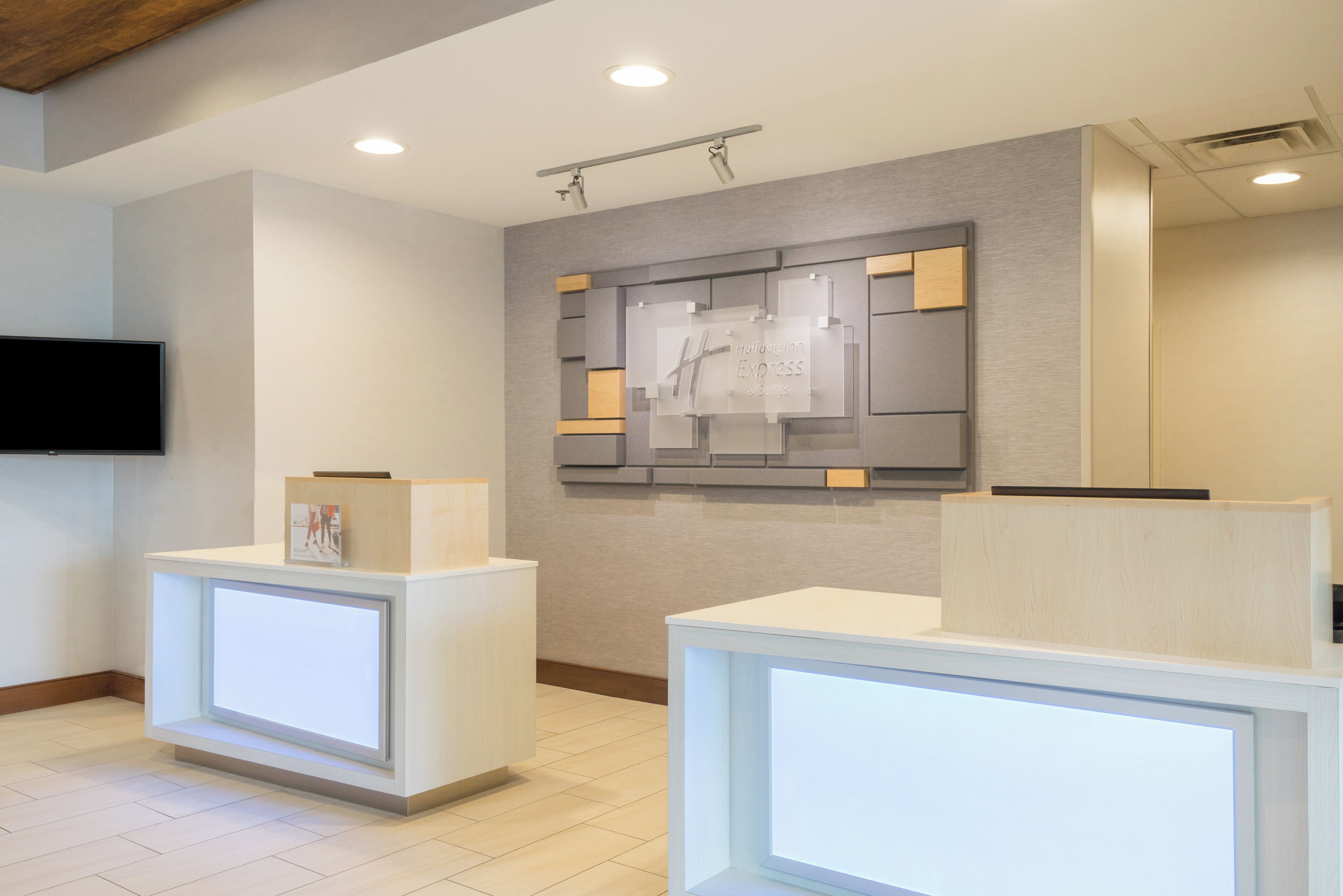 A hotel reception area with a flat-screen TV mounted on the wall, a reception desk, and a wall-mounted information board.