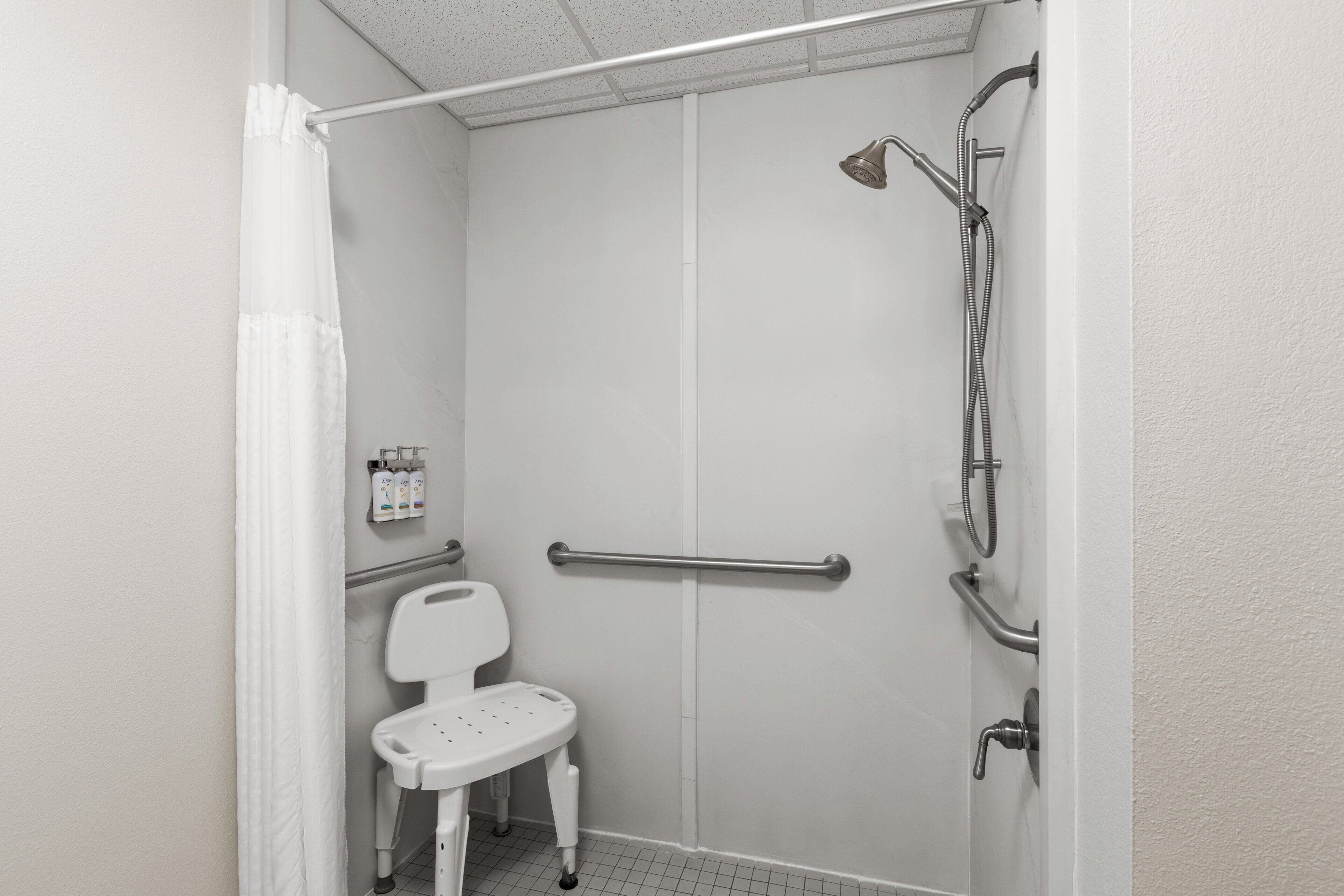 A small, enclosed shower area with a white toilet, grab bars, and a showerhead.
