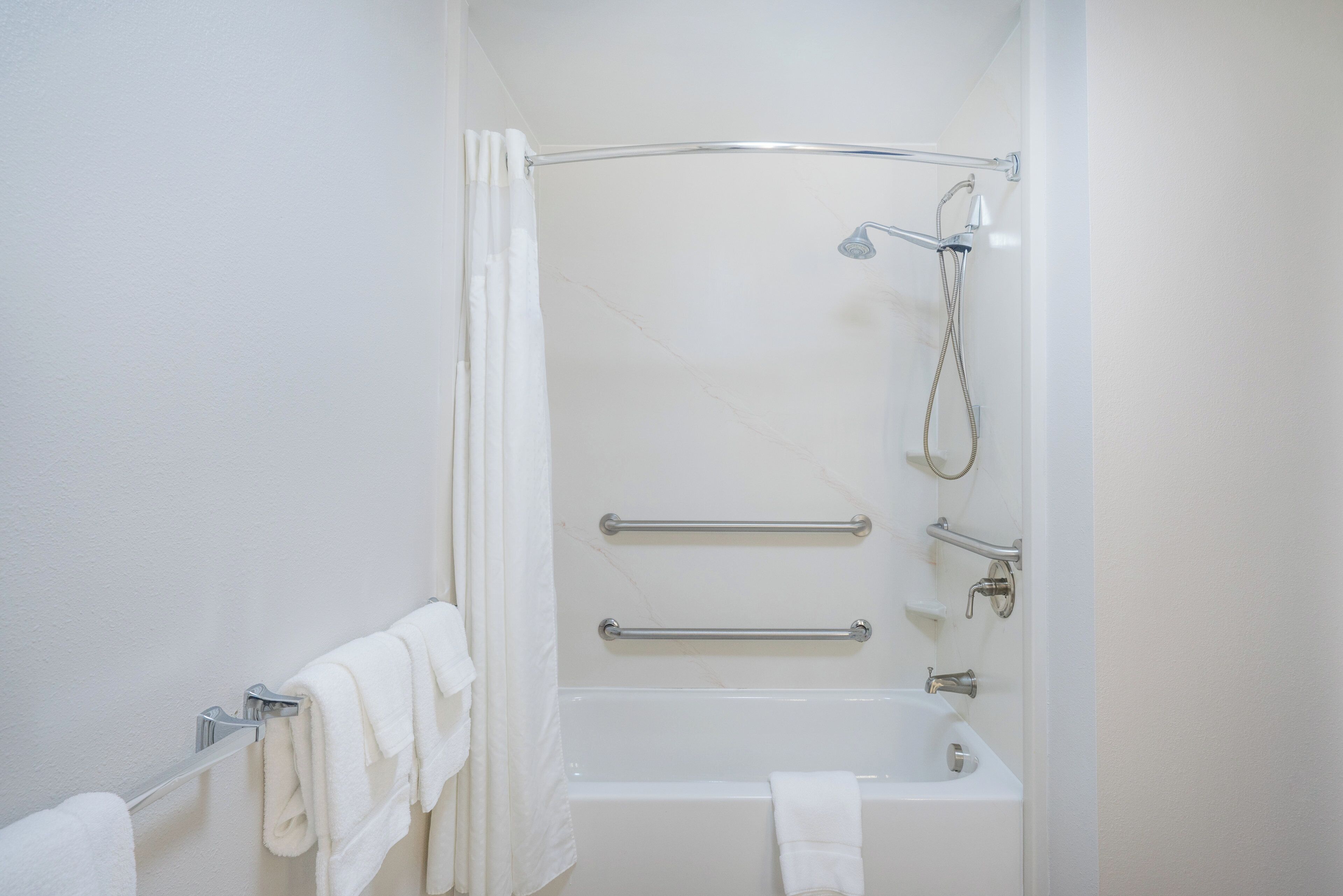 Un baño con bañera, ducha y barras de apoyo.